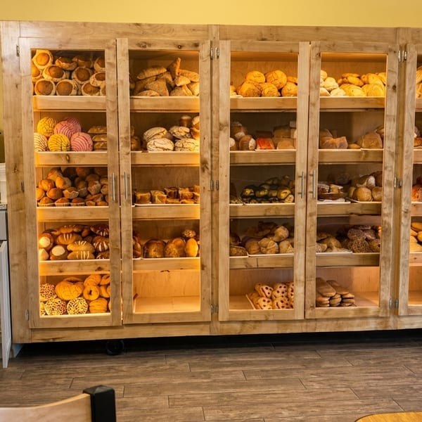 A person gets coffee next to a large wooden display case filled with various baked goods.
